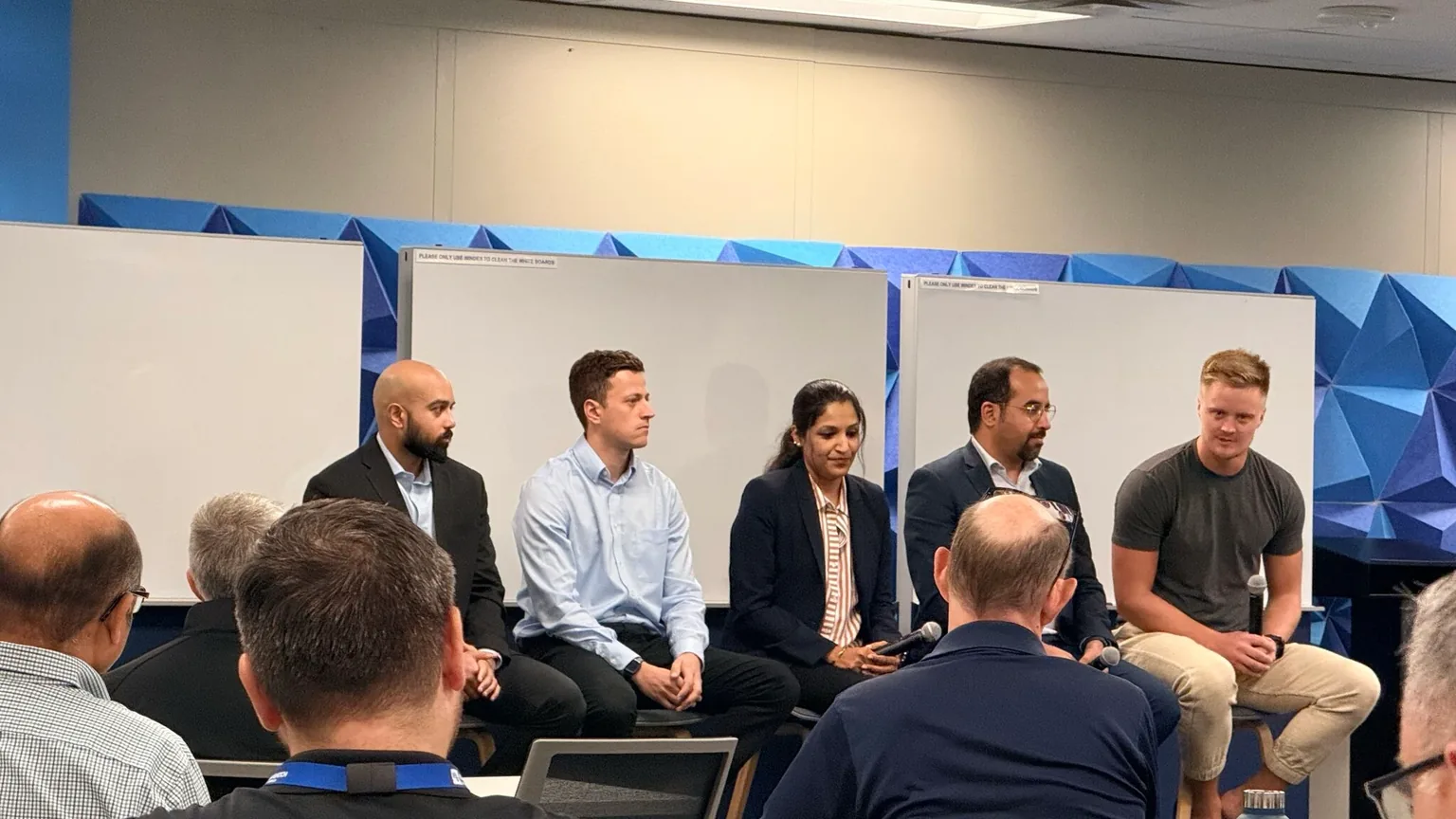 Five cohort company leaders seated on a panel in front of whiteboards, taking questions from a seated audience of Black and Veatch staff
